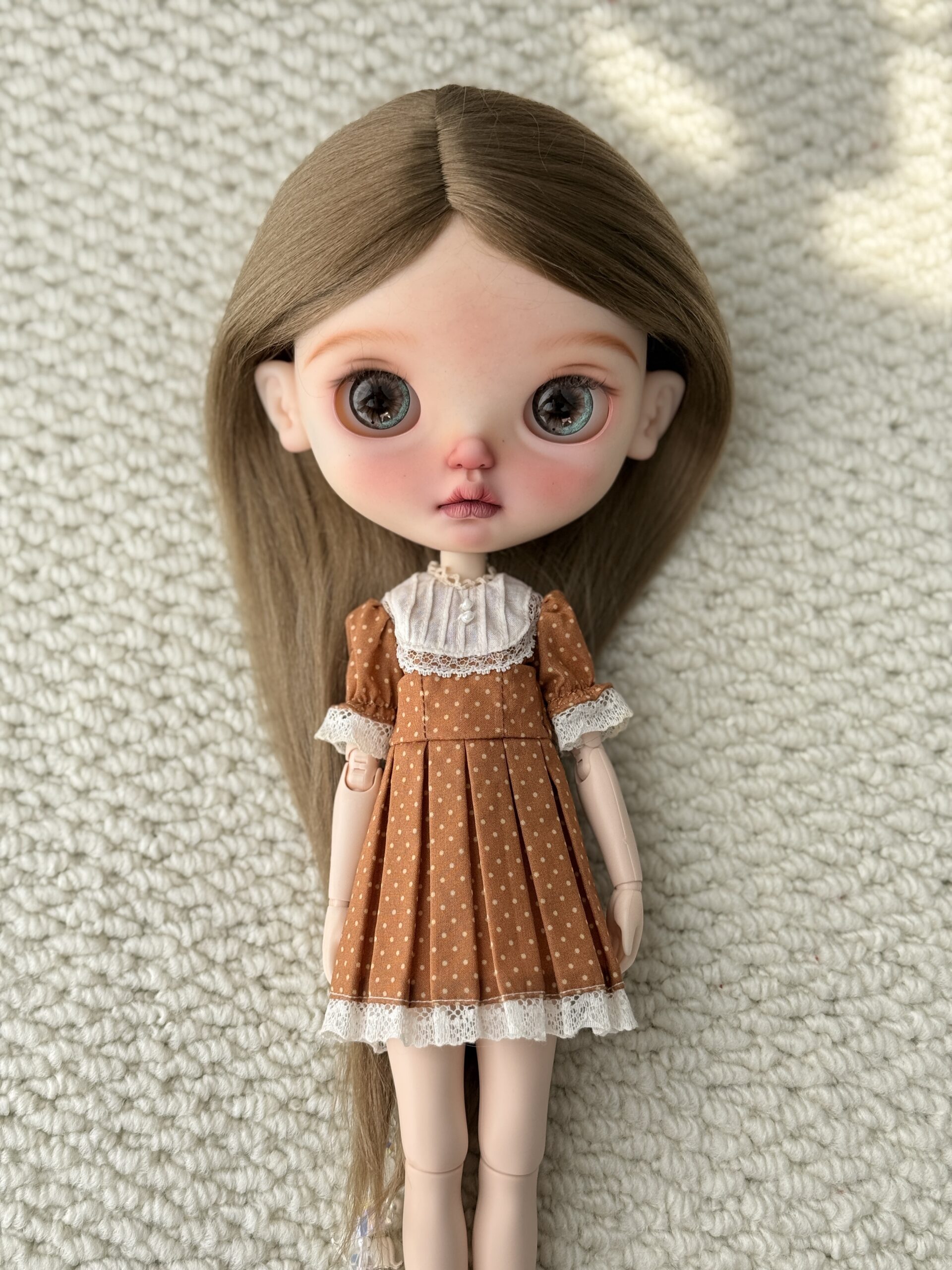 Doll wearing the Pumpkin Pintuck Vintage Dress with a cream pintuck bib, polka dots, and lace trim.