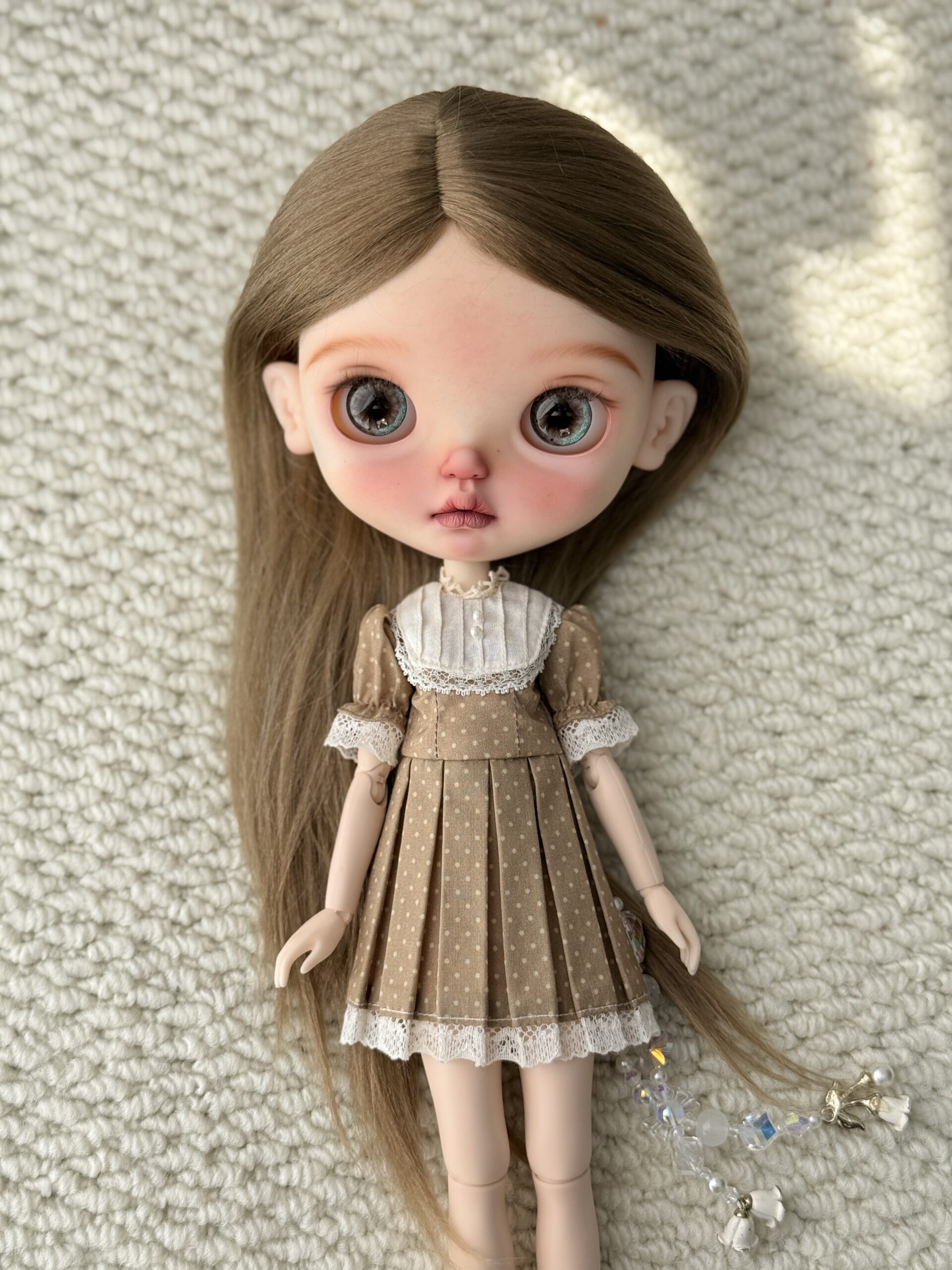 Doll wearing the Khaki Brown Pintuck Vintage Dress with a cream pintuck bib, polka dots, and lace trim.